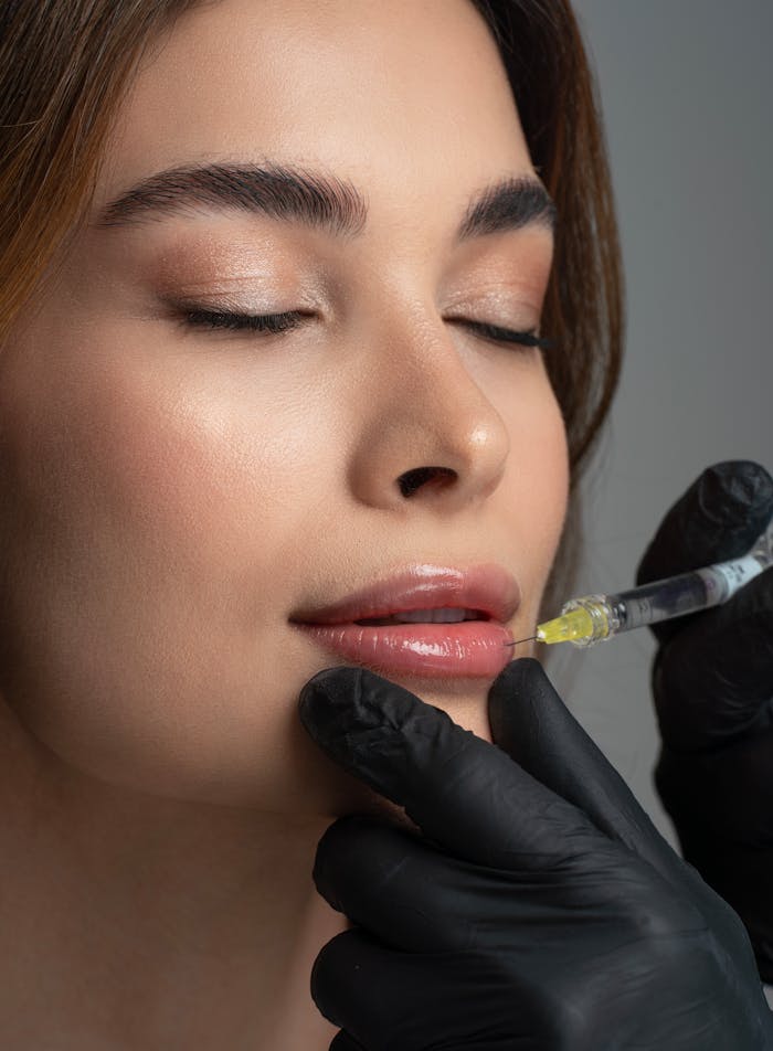A professional administering lip enhancement treatment to a woman with closed eyes, enhancing facial aesthetics.