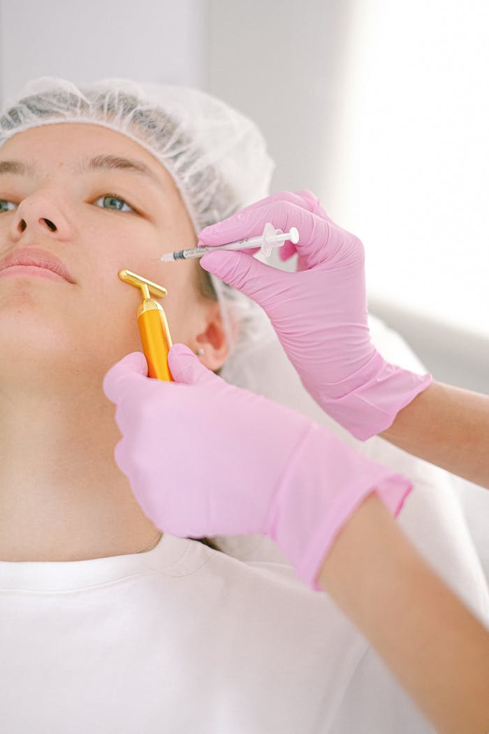 A woman receiving a cosmetic procedure with golden roller and syringe in a clinic.