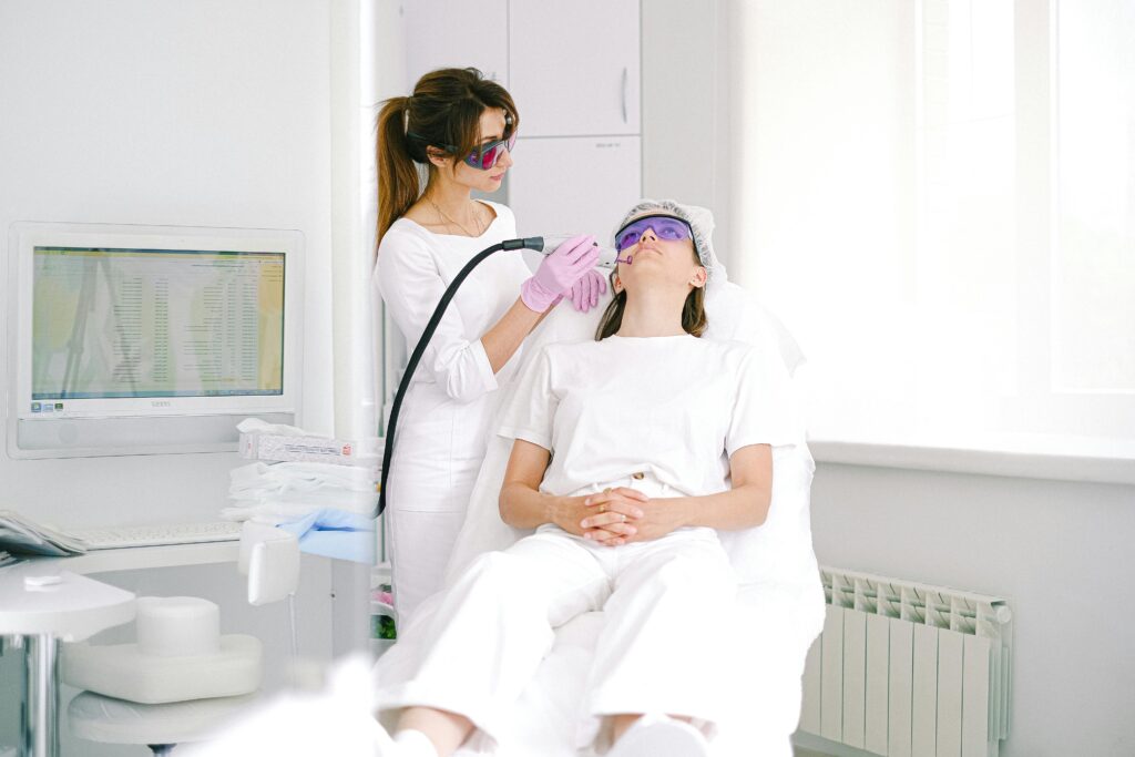 Aesthetician performing laser facial treatment on woman with protective eyewear in a modern clinic.